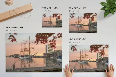 Plagát plachetnica pri západe slnka s pokojnou panorámou mesta